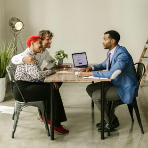 A travel agent in a blue suit consulting a smiling couple across a desk, highlighting personalized travel planning and client trust.